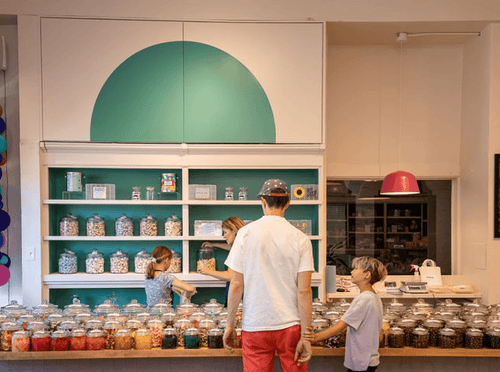Customers selecting pick-and-mix candy at the Candycopia counter in Oak Park, Illinois, with rows of glass candy jars